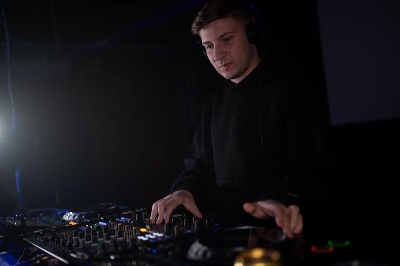 DJ in a black hoodie performing in low moody light